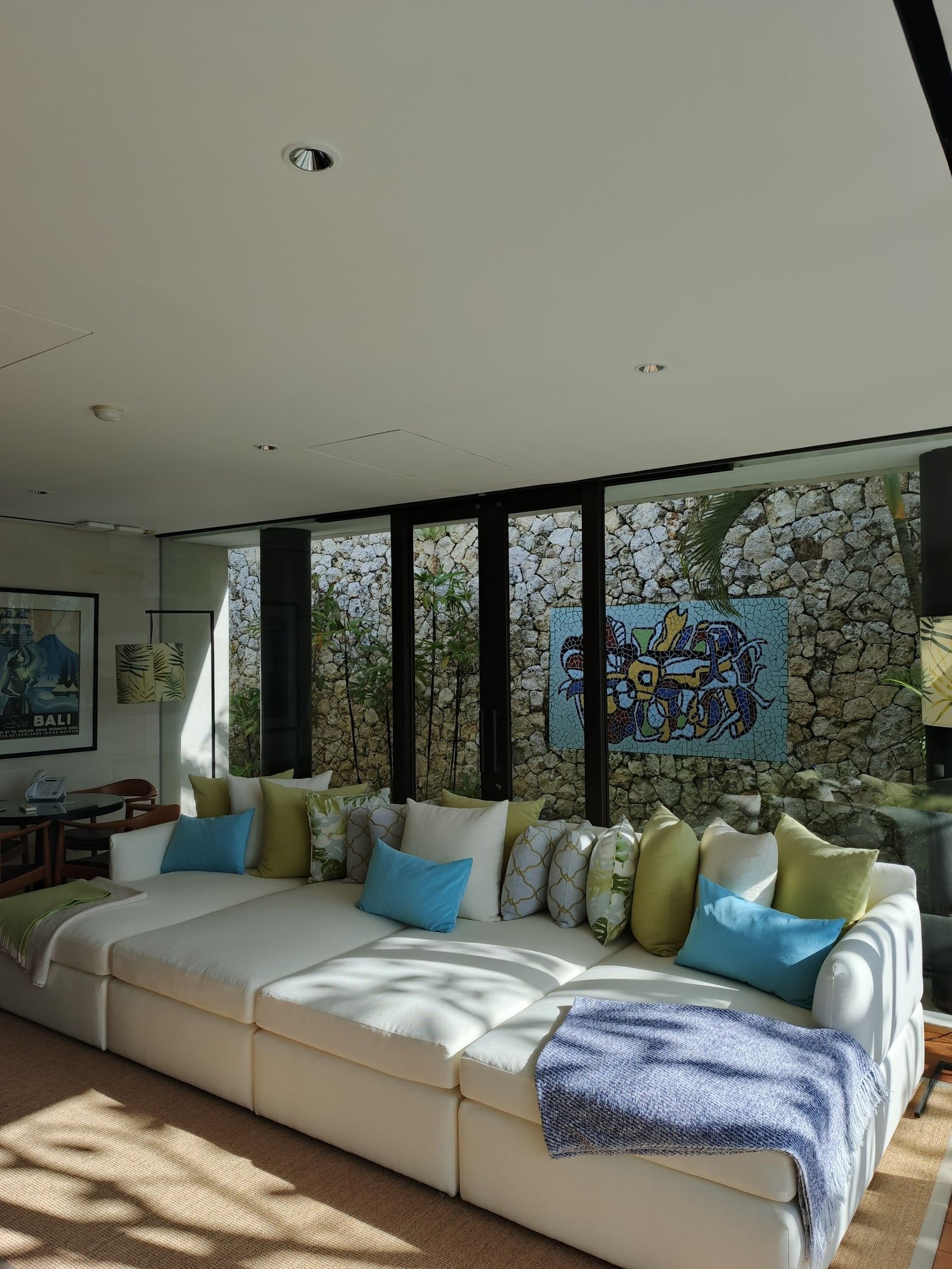 Long white modular sofa with blue and green cushions in front of a garden wall